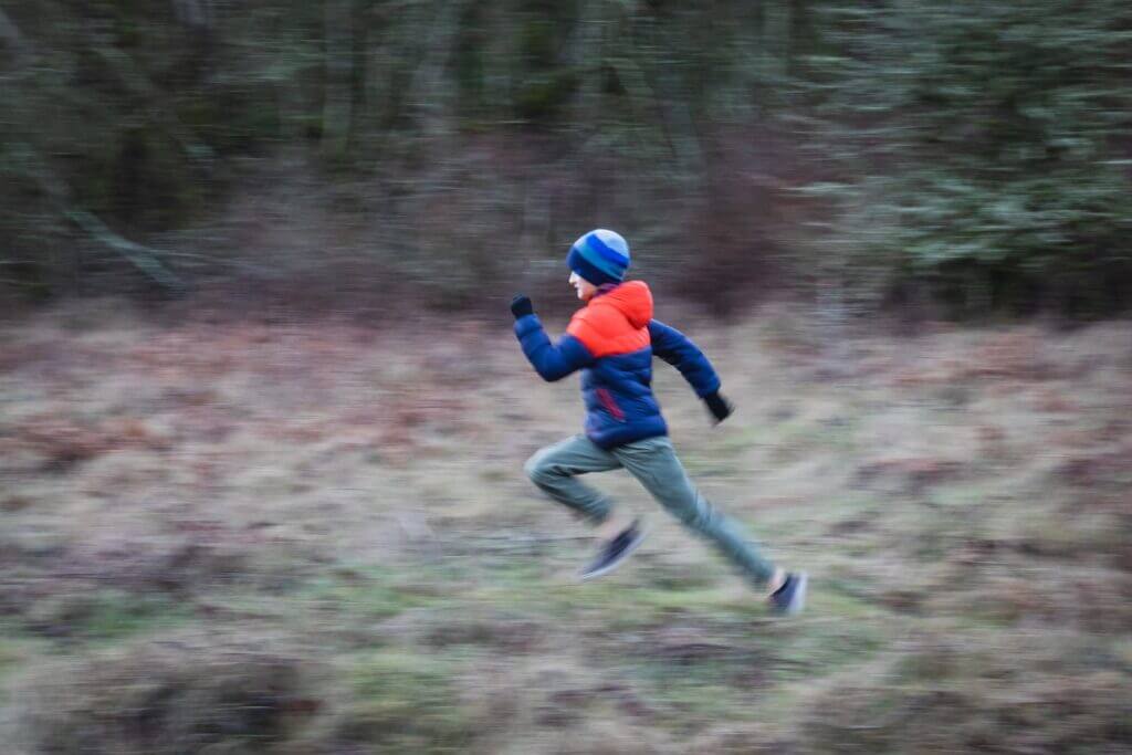 A child running very fast on a trail with an exaggerated arm swing motion