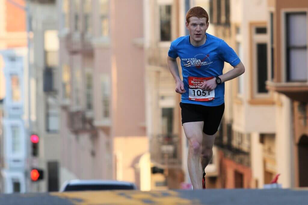 A man with ginger hair swinging his arms while running in the middle of the road for a marathon