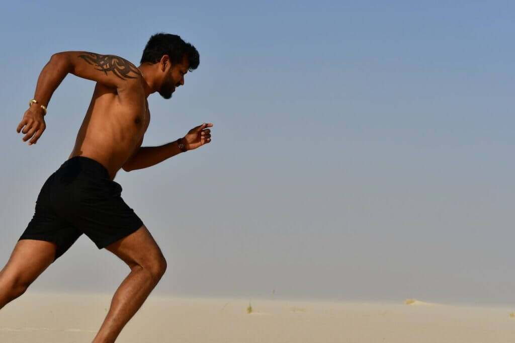A middle eastern young man running shirtless on the sand