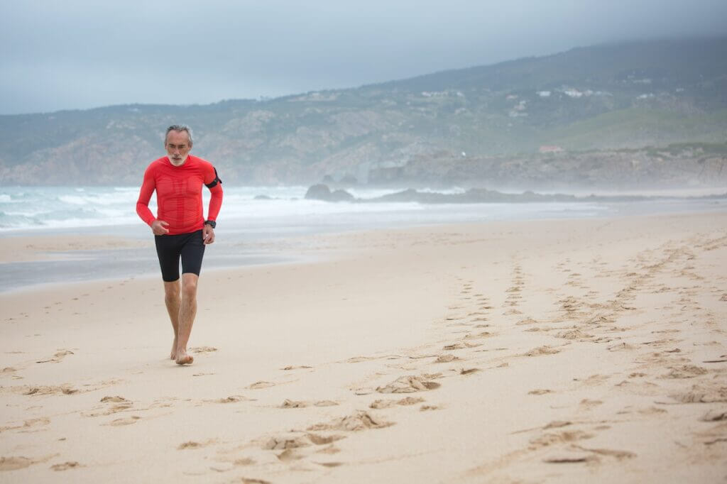 Old man with a red shirt running at the beach