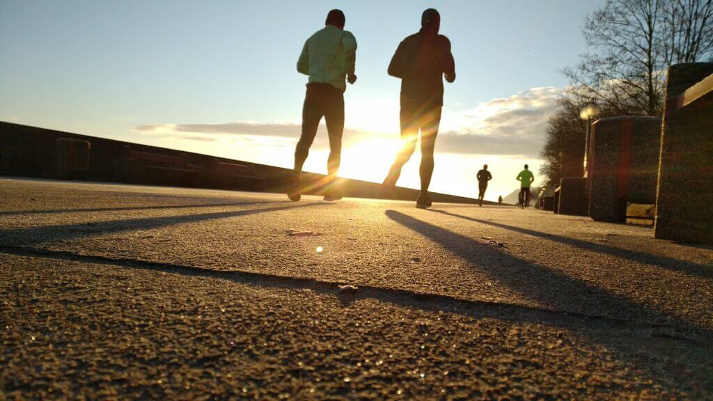 Two men running during the sunset on the side of the road