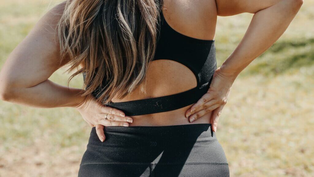 Woman with black running outfit putting her hands on her lower back because of an injury