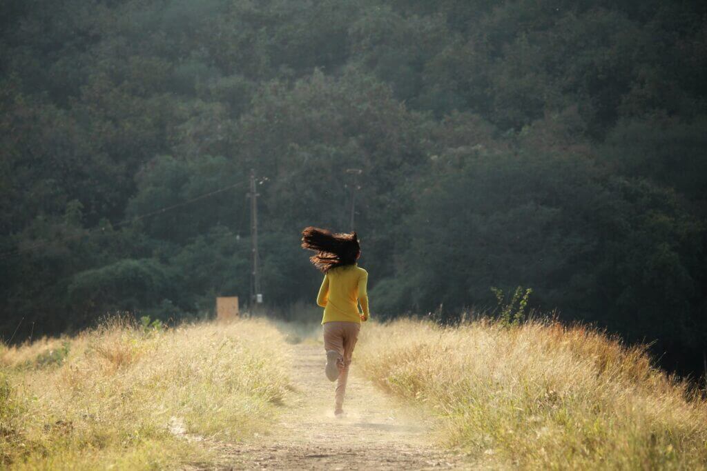 Back View of Woman Running at an average running speed on Footpath in Meadow with Tousled Hair