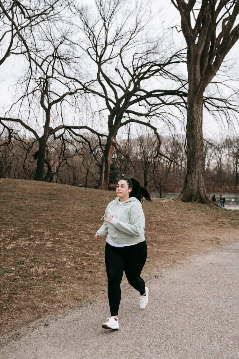Full body motivated plus sized female in gray hoodie running in autumn park