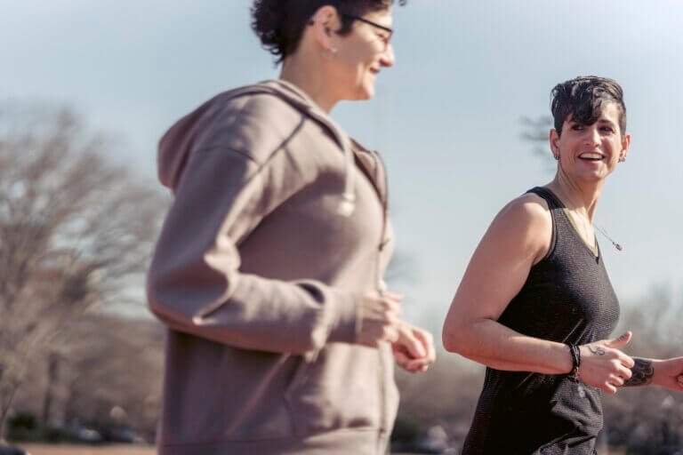 Side view of crop female athlete talking with smiling androgynous female while jogging to be in good shape and to keep healthy lifestyle