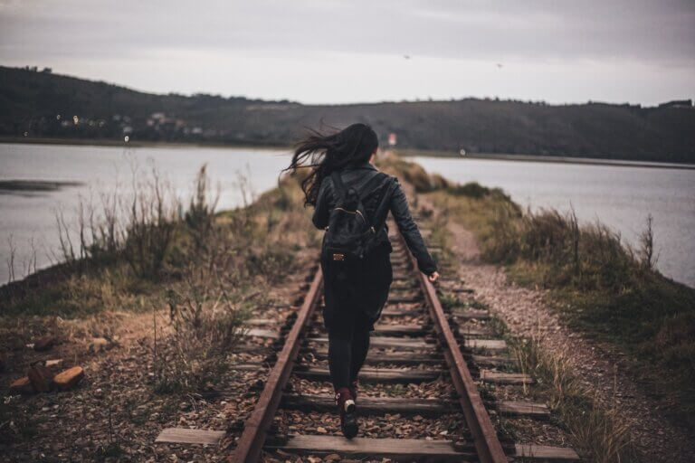 A Woman in Black Jacket running with a backpack on railways