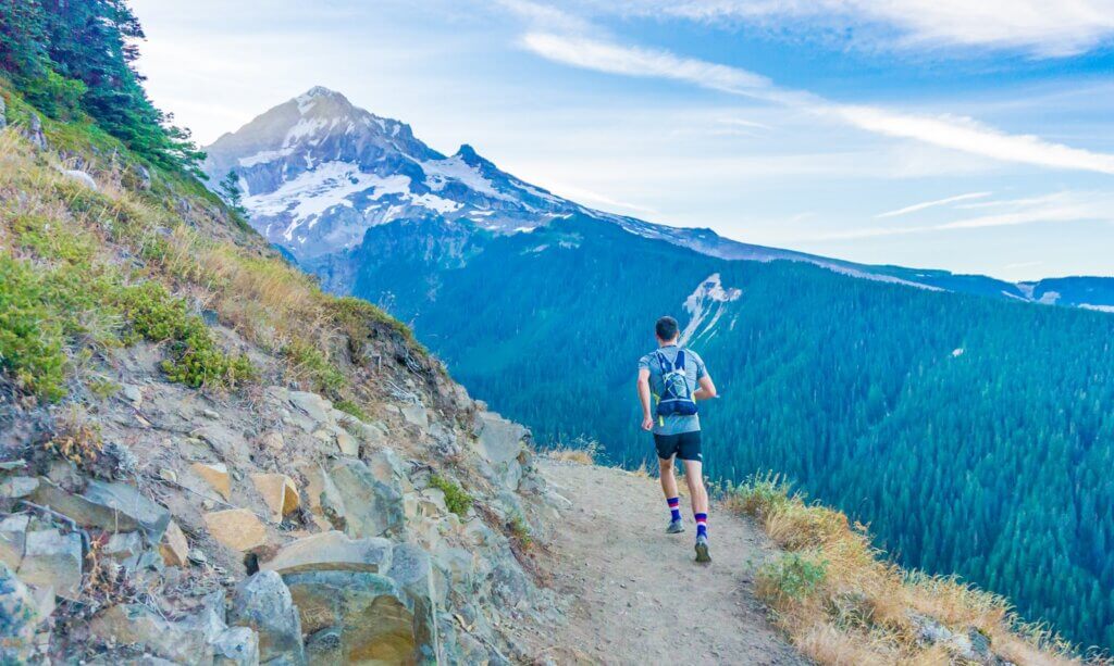 man running with a backpack on edge near mountain 