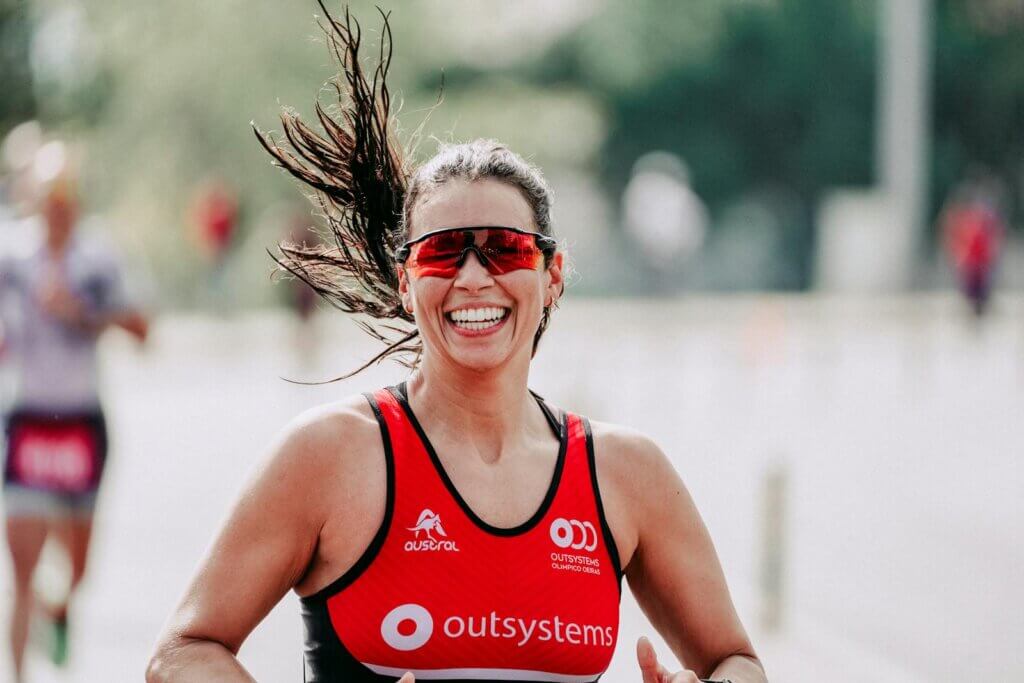 Happy female athlete in sportswear and protective glasses smiling while running on road during competition